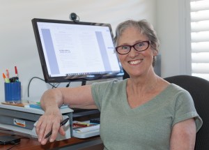 Photo of Teena Raffa-Mulligan in a grey shirt sitting at her computer desk.