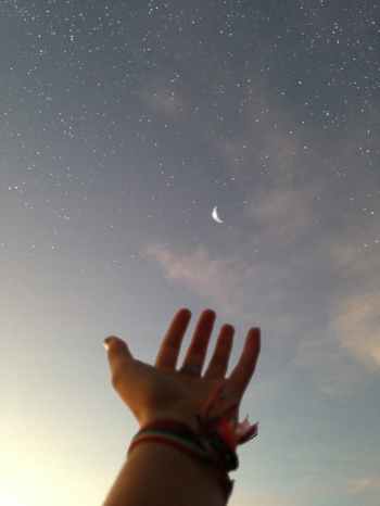 A hand with palm up towards a crescent moon and stars in a pale evening sky. Photo courtesy of pexels.com
