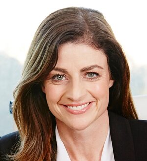 Image shows a headshot photo of author Kim Doherty. Kim has medium-long straight brown hair, fair skin, and pale eyes. She's wearing a white shirt and a black jacket. She's smiling directly into the camera.