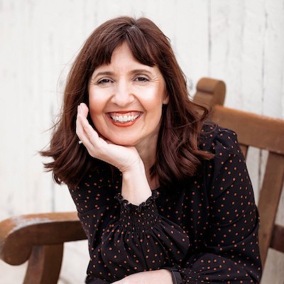 Image shows a photo of Sharon Giltrow, children's author. Sharon has shoulder length brown hair, fair skin and brown eyes. She's wearing a black shirt with tan dots. She's sitting with her chin in one hand.