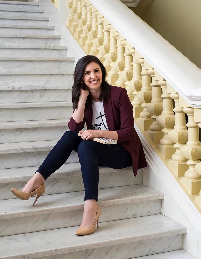 Author and journalist Chenée Marrapodi, sits on marble steps with a book on her lap.