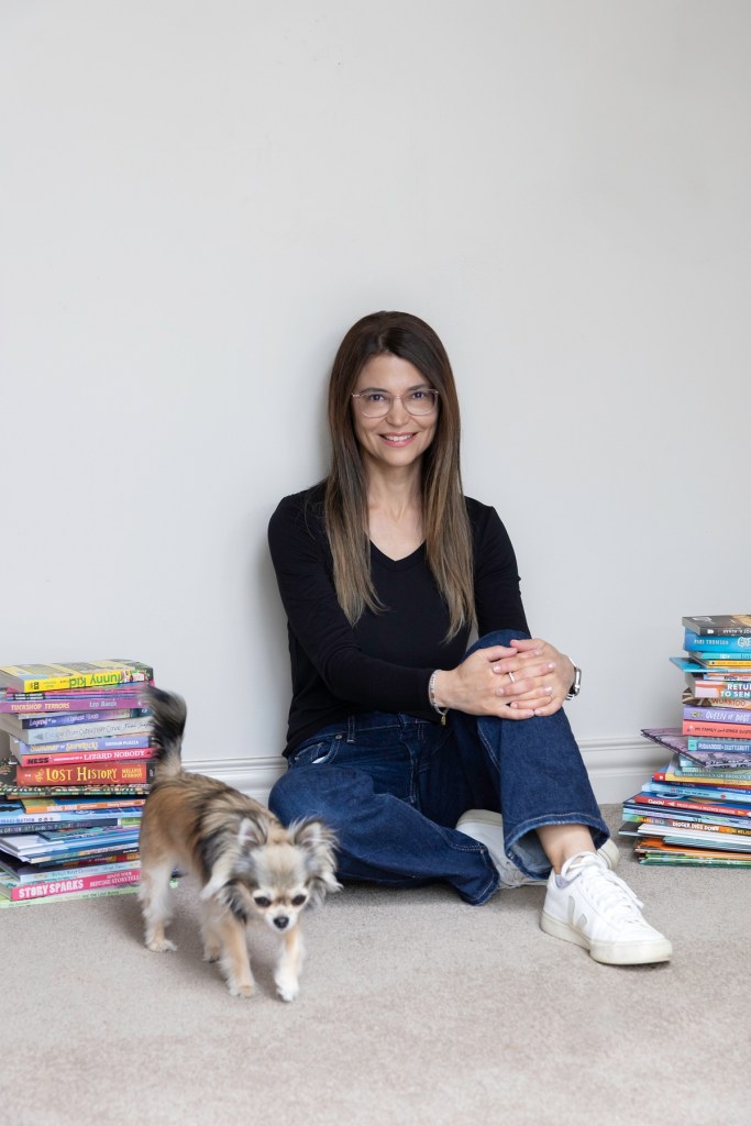 A woman surrounded by books and a small dog.