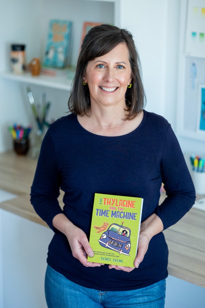 René Treml standing in an art studio holding a book for children.
