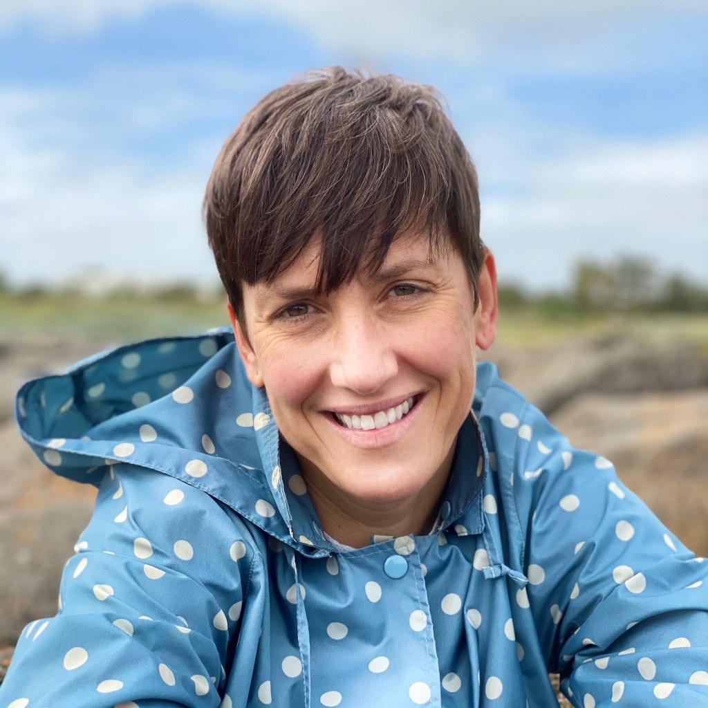 A photo of a woman with a pixie cut, wearing a blue raincoat with white spots. 